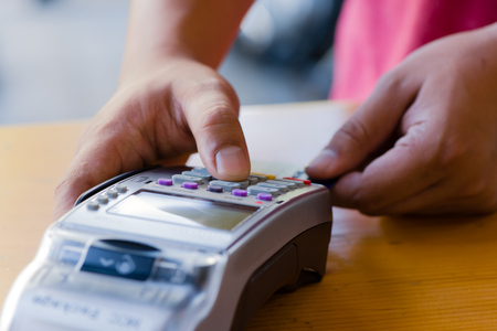 close up customer hand holding and paying for order by credit card in cafe and restaurant.credit card payment service.custumer or waiter typing code on credit card swipe machine.paying process.の写真素材