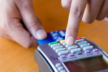 close up customer hand holding and paying for order by credit card in cafe and restaurant.credit card payment service.custumer or waiter typing code on credit card swipe machine.paying process.の写真素材