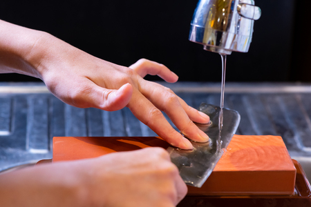 woman professional chef hands hold knife for whetting on whetstone.premium professional stone from japan.knife sharpening process with traditional sharpener stone for knife sharpen edge in restaurant.の写真素材
