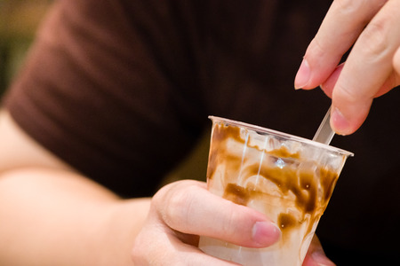close up eat out vanilla ice cream with chocolate fudge in cup.hands man eating ice cream vanilla with chocolate fudge on top.tasty sweets vanilla ice cream and chocolate fudge in fast food.の写真素材