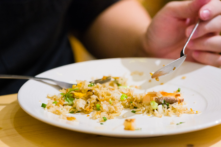 fried sliced salmon with fried rice.man hands use fork and spoon for fusion food.sliced salmon with rice on white plate in restaurant or cafe.man sitting and eating sliced salmon on laptop backgroundの写真素材