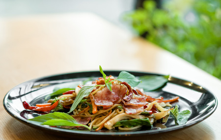 delicious spicy spaghetti dried chilli and basil sauce with bacon and mushroom ,beautiful close up spicy spaghetti bacon on black plate with some space for text.の写真素材