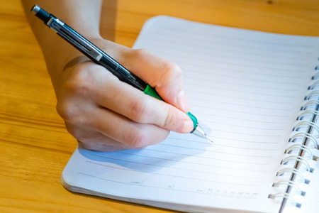 female hand with pencil writing on notebook at coffee shop.woman working by hand writing on letter...