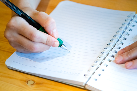 female hand with pencil writing on notebook at coffee shop.woman working by hand writing on letter paper on the wooden desk.woman hand writing.の写真素材