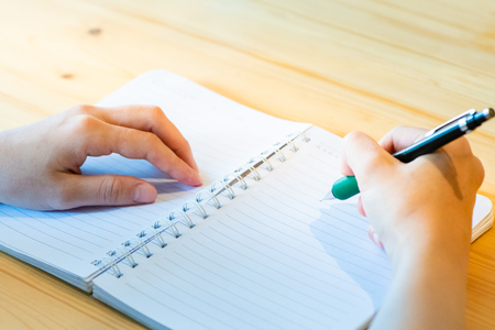 female hand with pencil writing on notebook at coffee shop.woman working by hand writing on letter paper on the wooden desk.woman hand writing.の写真素材