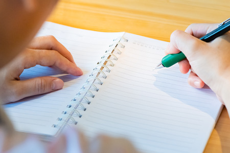 female hand with pencil writing on notebook at coffee shop.woman working by hand writing on letter paper on the wooden desk.woman hand writing.の写真素材