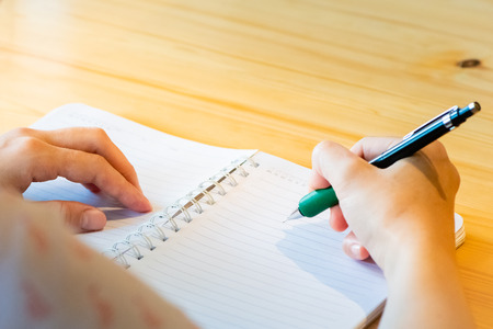 female hand with pencil writing on notebook at coffee shop.woman working by hand writing on letter paper on the wooden desk.woman hand writing.の写真素材