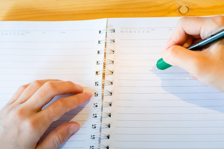 female hand with pencil writing on notebook at coffee shop.woman working by hand writing on letter paper on the wooden desk.woman hand writing.の写真素材