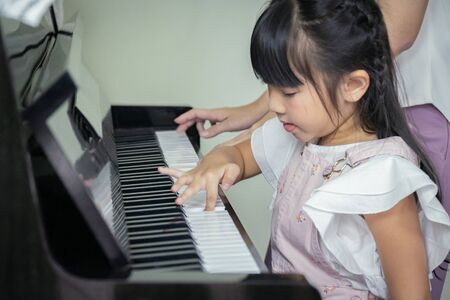 Happy mother and daughter playing a black grand paino together in a house.の写真素材