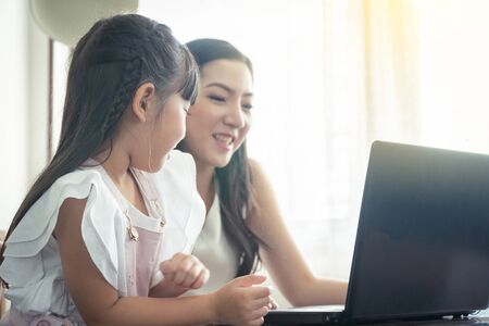 Beautiful asian mother and daughter working together at home office by the window. in concept of single mom or single parent.の写真素材