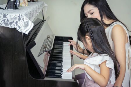 Happy mother and daughter playing a black grand paino together in a house.の写真素材