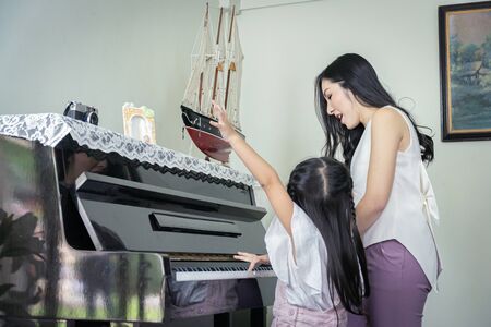 Happy mother and daughter playing a black grand paino together in a house.の写真素材