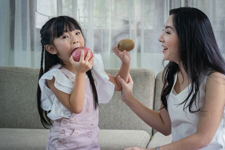 Happy together! Asian mother and her daughter funny together with their fruits at sofa. single mom concept.の写真素材