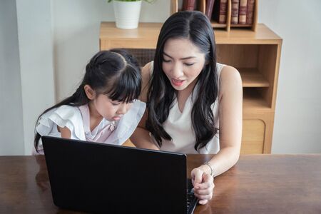 Beautiful asian mother and daughter working together at home office by the window. in concept of single mom or single parent.の写真素材