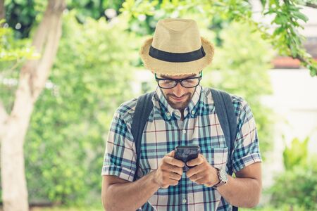 Happy young bearded wearing eye glasses man carrying his backpack preparing to travel. searching the map on mobile phone.の写真素材