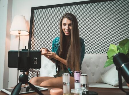 Young beauty blogger selling her cosmetic on live stream broadcasting by mobile phone.の写真素材