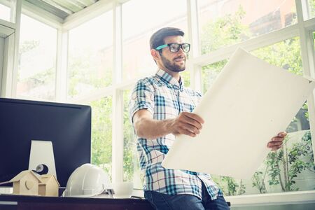 Young caucasian holding his blueprint project at the desk in home office.の写真素材