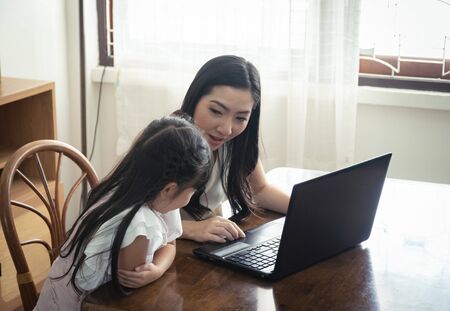 Beautiful asian mother and daughter working together at home office by the window. in concept of single mom or single parent.の写真素材