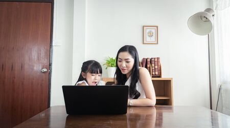 Beautiful asian mother and daughter working together at home office by the window. in concept of...