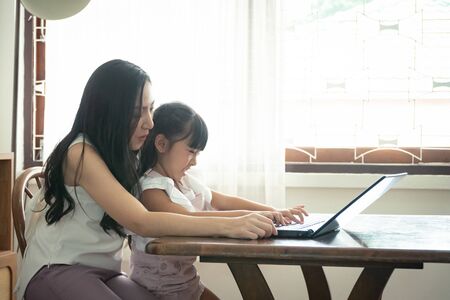 Beautiful asian mother and daughter working together at home office by the window. in concept of single mom or single parent.の写真素材