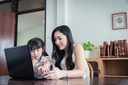 Beautiful asian mother and daughter working together at home office by the window. in concept of single mom or single parent.の写真素材