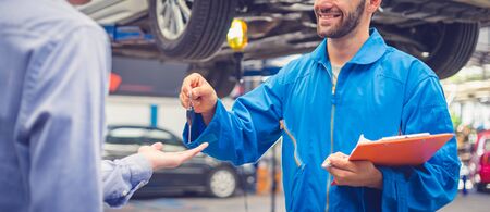 Mechanic holding clipboard giving the key back to car owner in the workshop garage. Car auto services conceptsの写真素材