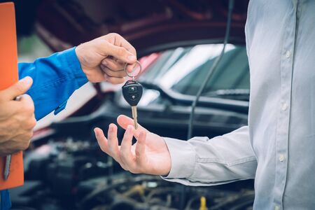 Mechanic holding clipboard giving the key back to car owner in the workshop garage. Car auto services conceptsの写真素材
