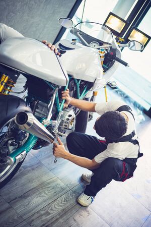 Asian mechanic man fixing the retro motorcycle in the garage. Film effected - Selective focusedの写真素材