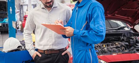 Mechanic holding clipboard with car owner in the workshop garage. Car auto services conceptsの写真素材