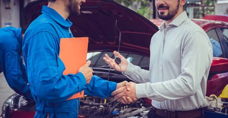 Mechanic holding clipboard shaking hands with car owner in the workshop garage. Car auto services conceptsの写真素材