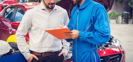 Mechanic holding clipboard with car owner in the workshop garage. Car auto services conceptsの写真素材