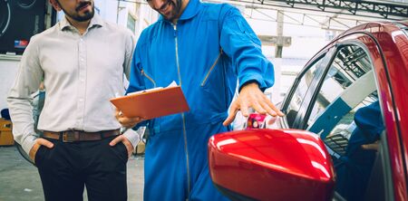 Mechanic holding clipboard with car owner in the workshop garage. Car auto services concepts