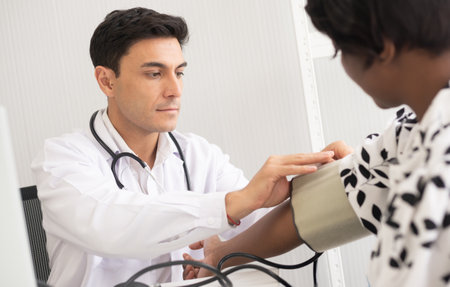 Hispanic doctor measuring African American patient's blood pressure. Person medical healthcare and wellbeing, the physician meet with patient at clinic concept.の写真素材