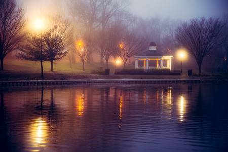 Foggy night scene at pond with lights and gazeboの写真素材
