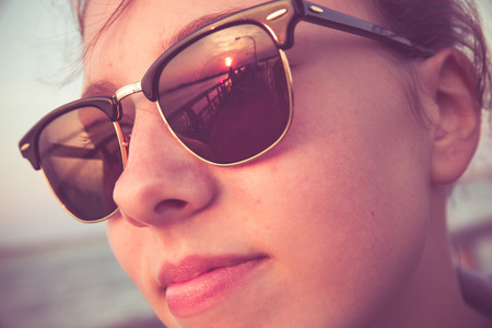Cute teenage girl with sunset reflections in sunglasses. Image has a retro vintage filter effect.の写真素材