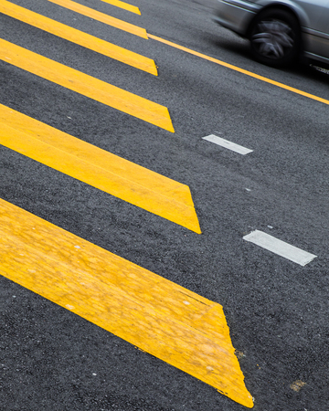 Yellow painted crosswalk road line markings with moving car in background