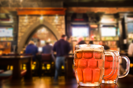 Two glass mugs of cold bar in a typical Irish pub setting with blur of people in the backgroundのeditorial素材