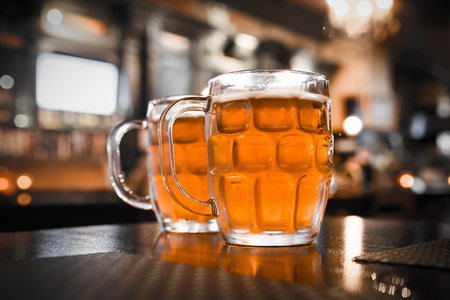 Two glass mugs of cold bar in a typical Irish pub setting with blur of people in the backgroundの写真素材