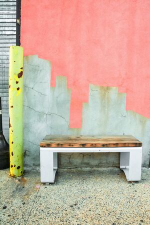 Bench on sidewalk against colorfully painted cement cracked wall.の写真素材