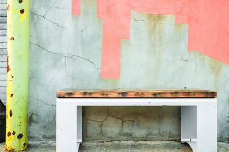 Bench on sidewalk against colorfully painted cement cracked wall.の写真素材