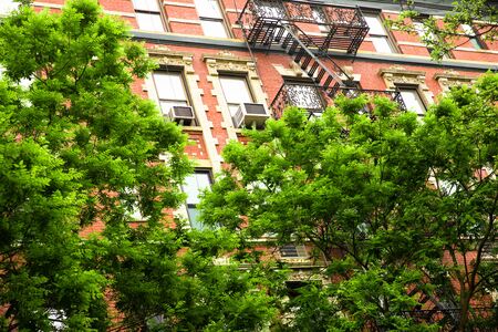 Typical New York City brick apartment building in spring surrounded by green trees.