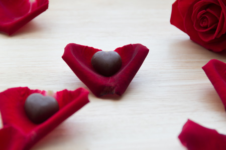 red rose with chocolate in petals on wood tableの写真素材