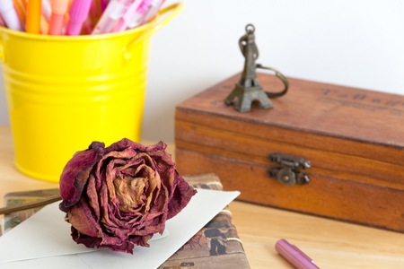 dry rose on a letter and pink pen with Eiffel tower key chain on  wood box and yellow pen cupの写真素材