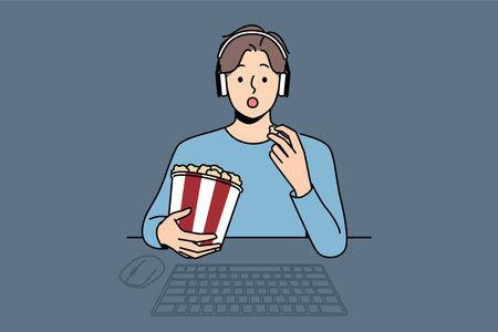 Man with popcorn watches movie sitting at table with computer and looks at screen intriguedのイラスト素材