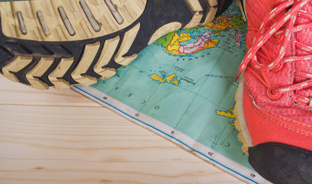 Top view of travel accessories for a mountain trip on old wooden background : hiking boots, and map. Selective focus on tread of the bootsの写真素材