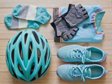 Top view of sport equipment in pastel colour: helmet, shoes, biking clothes, biking gloves, socks, and notebook on wooden backgroundの写真素材