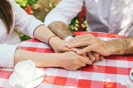 Closeup image of a young couple holding hands, having a date in a cafe. against the background of the red tableの写真素材