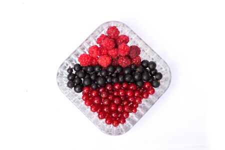 set of fresh berries of currant and raspberry in a plate on a white backgroundの写真素材