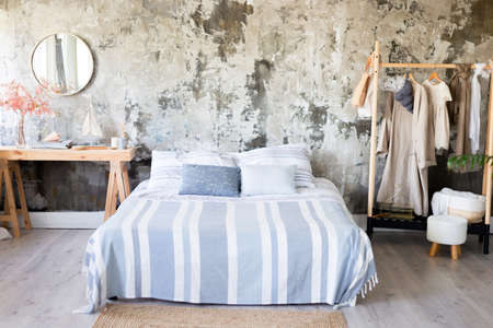 area for a loft-style photo shoot in bright colors. A stylish modern bed with interior details with a textured gray wall. Boho style. a hanger with clothes and a table with a mirror.の写真素材