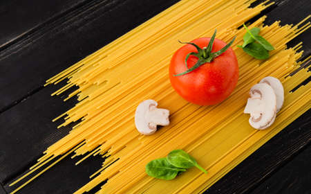 Spaghetti with tomato, mushrooms and spinach on black background. Top view. Healthy eating concept. Preparation of productsの写真素材